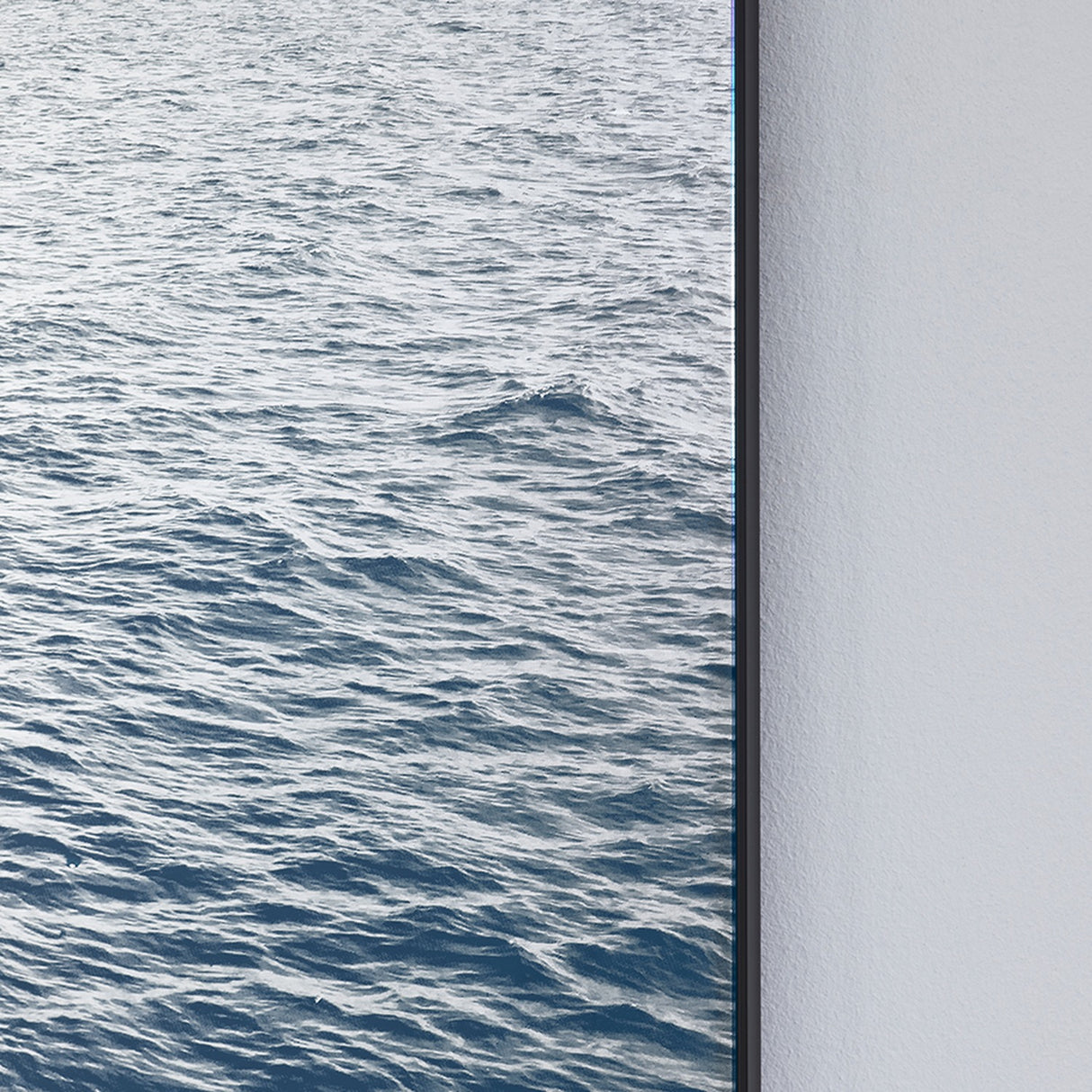 Maro Seascape Printed Glass Wall Mirror 120cm, close-up of the rectangular black-framed edge showing printed blue seascape against a plain light grey wall.