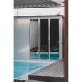 Three Lucka full length garden mirrors with slim black metal frames mounted on an outdoor wall beside a swimming pool, reflecting the poolside setting.