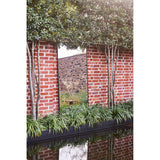 Lucka Outdoor XL full length garden mirror, 175cm, slim black metal frame, mounted on a red brick wall reflecting trees and greenery.