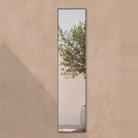 Slim full length outdoor mirror in a satin black frame on a terracotta plaster garden wall, reflecting an olive tree.