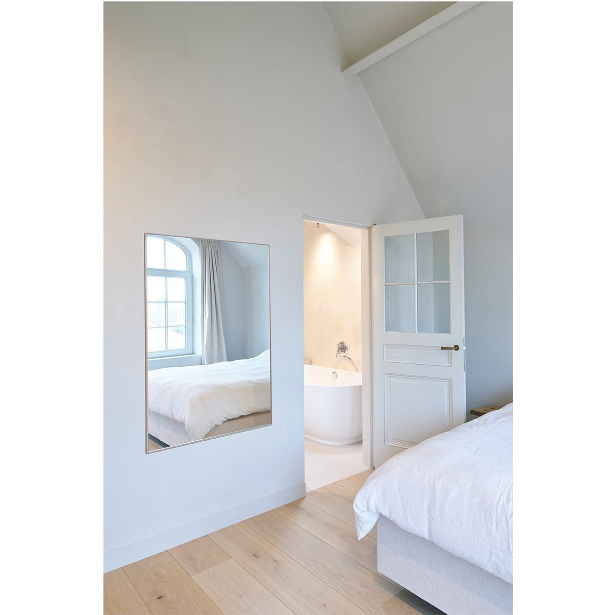 Lucka Solid Oak Full Length Mirror in a bedroom, rectangular wall mirror with slim oak frame reflecting a bed and arched window.