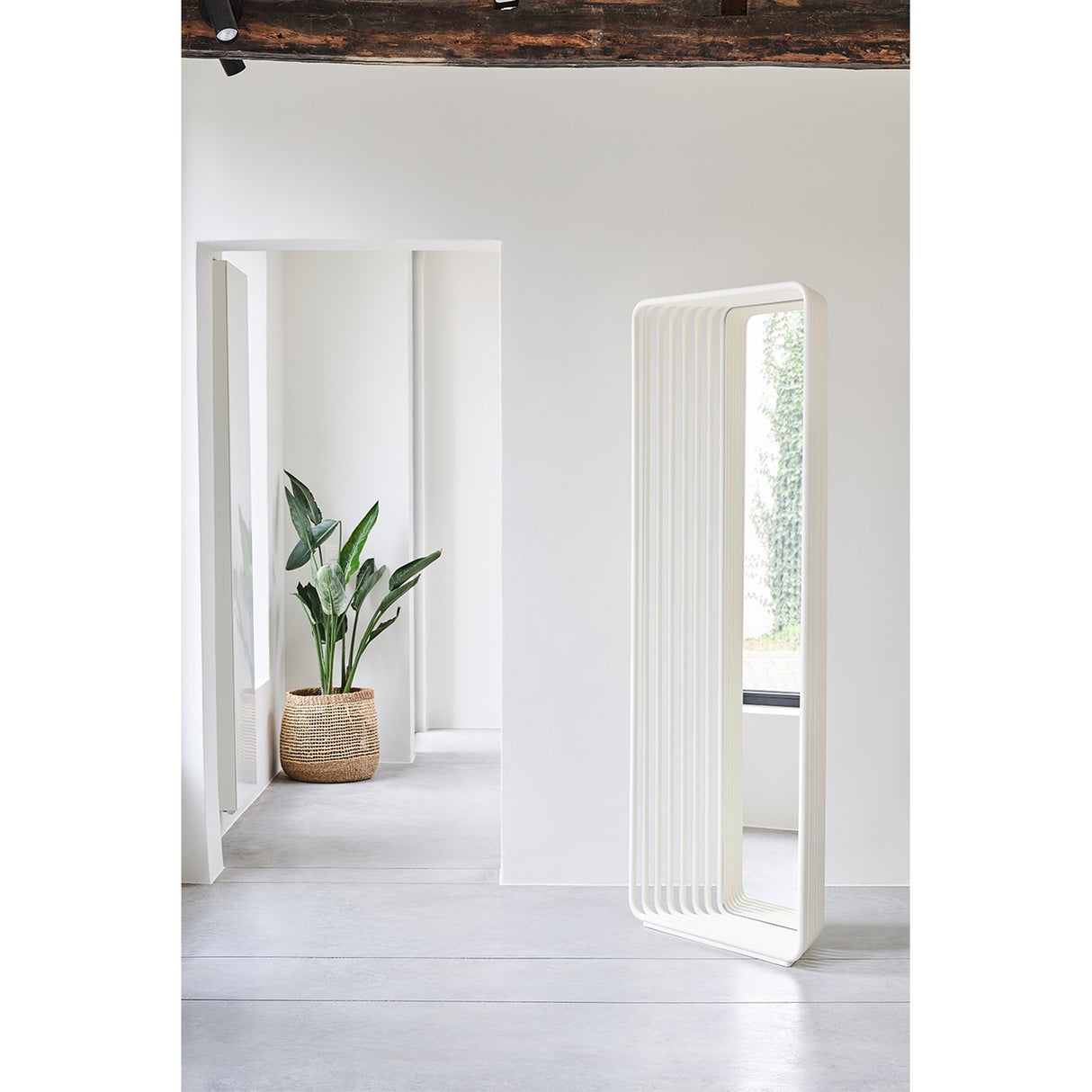 Echo White free standing cheval mirror, 193cm, with stacked white powder-coated metal slats curving into a base, shown in a bright hallway near a plant.