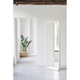 Echo White free standing cheval mirror, 193cm, with stacked white powder-coated metal slats curving into a base, shown in a bright hallway near a plant.