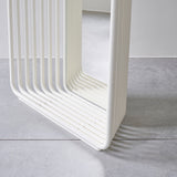 Close-up of the Echo White free standing mirror's base, showing stacked white powder-coated metal slats curving round with a mirrored panel between, set on a concrete floor.