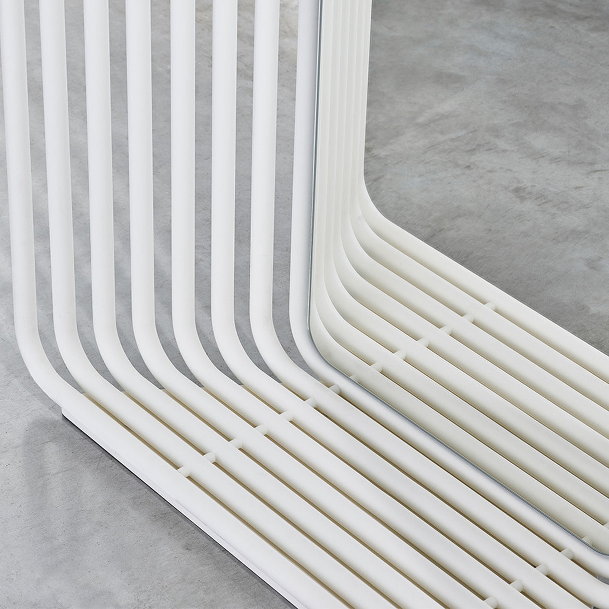 Close-up of the Echo White Double Sided Free Standing Mirror, showing white powder-coated metal slats curving at the base around a mirrored panel, set on a concrete floor.