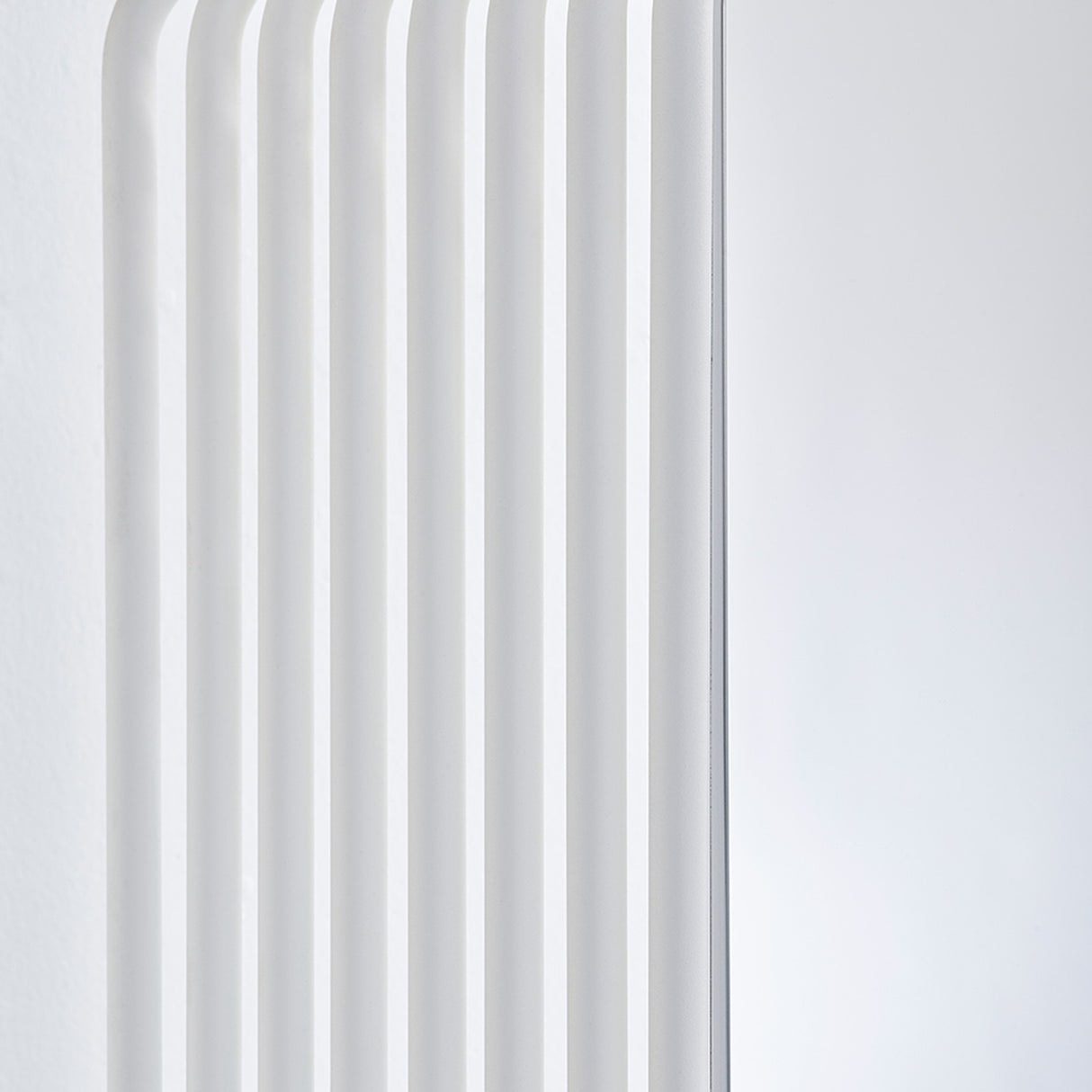 Close-up of the Echo White Free Standing Mirror's edge, showing stacked white powder-coated metal slats with gaps and a curved base against a plain light background.
