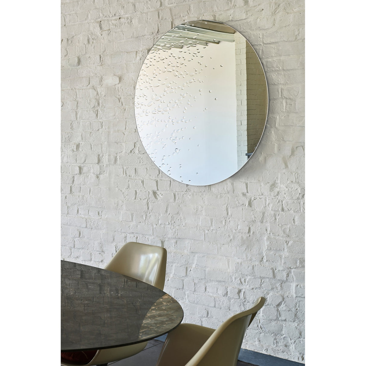 Matin frameless round wall mirror, 100cm, with hand-applied dewdrop texture across the glass, shown above a dining table in a whitewashed brick room.