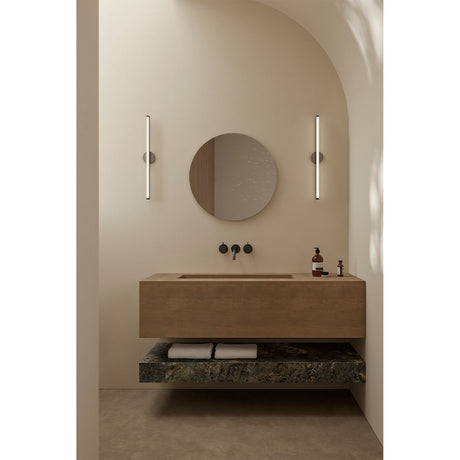 Matin 60cm round frameless wall mirror with hand-applied dewdrop detail, mounted above a wood vanity between two vertical LED wall lights in a bathroom.