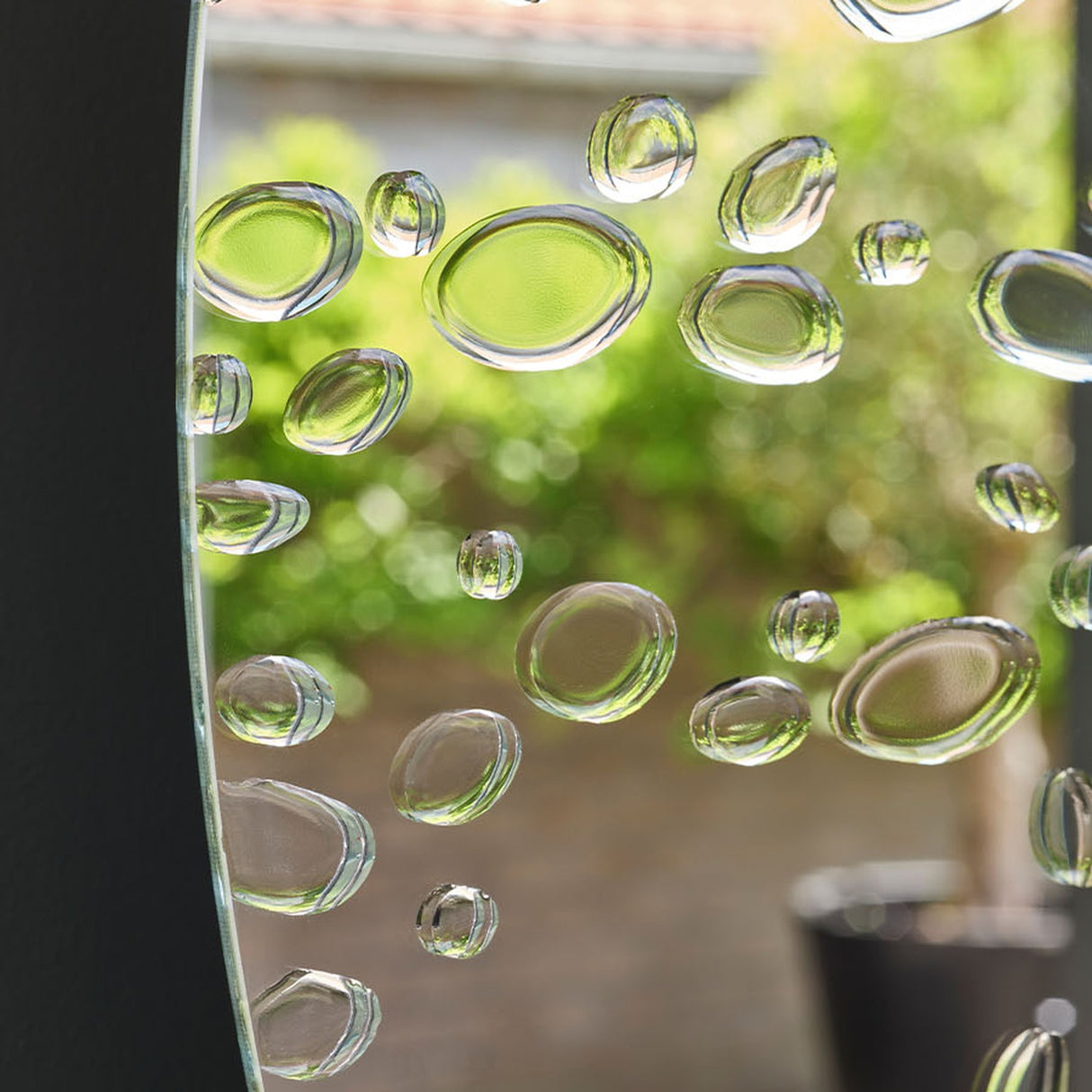 Matin round wall mirror 60cm, frameless glass with hand-applied raised dewdrop details, reflecting a sunlit garden scene.