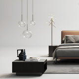 A modern bedroom showcases a brown upholstered bed with gray bedding. A dark wooden nightstand, adorned with decorative vases and books, is complemented by elegant pendant lights. The Solarae Floor Lamp - Brass, featuring an antique brass finish and clear blown glass diffusers, stands nearby.