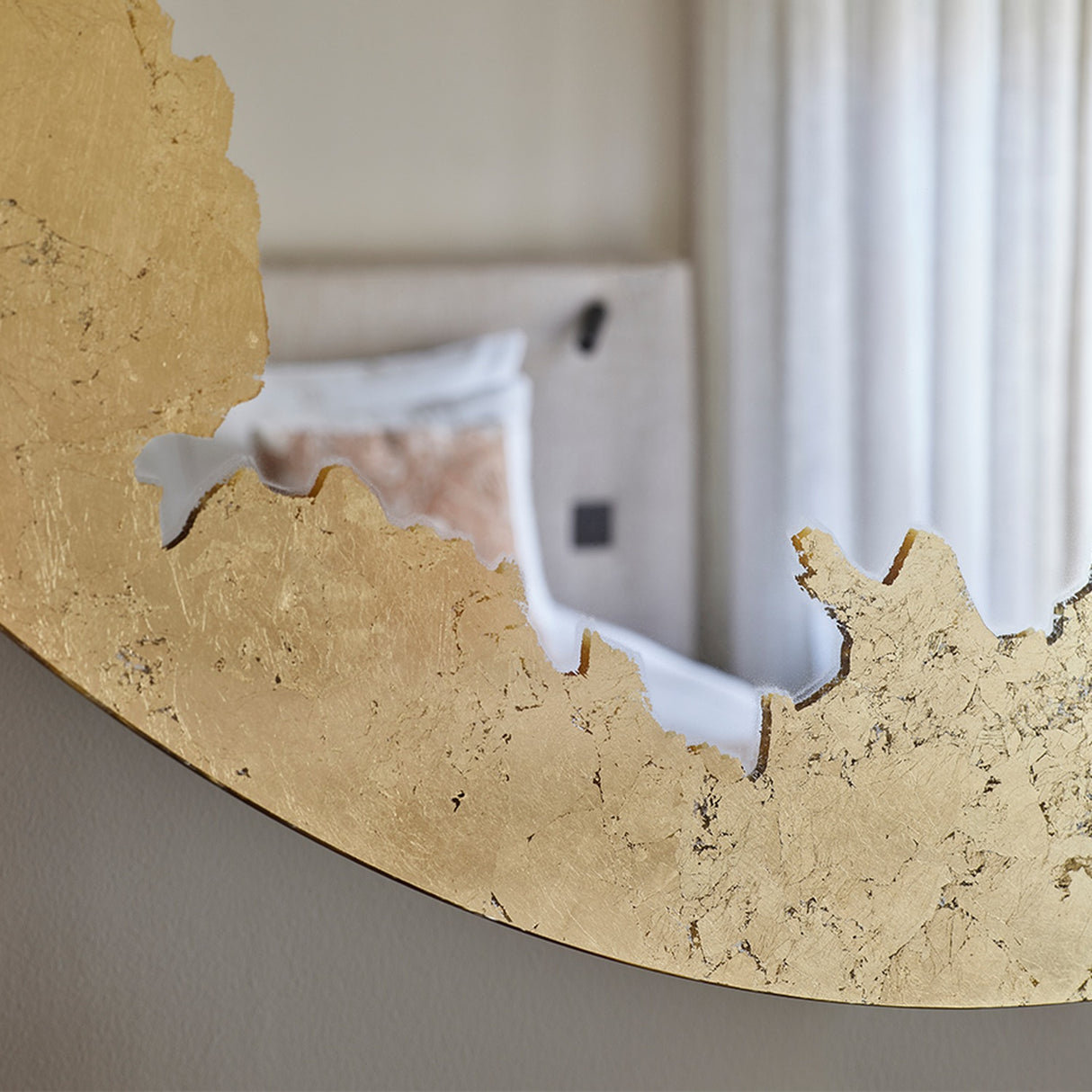 Close-up of the Ornato Gold Leaf Round Rotating Wall Mirror 70cm, showing the hand-applied gold leaf's torn edge against the plain glass, set in a bedroom.