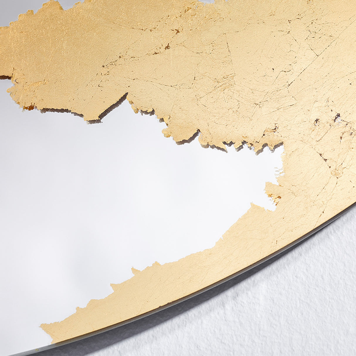 Close-up of the Ornato Gold Leaf Round Rotating Wall Mirror 70cm, showing hand-applied gold leaf with a torn, irregular edge against the plain mirror surface.
