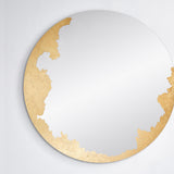 The gilded round mirror seen straight on, the hand applied gold leaf gathered down one side of the glass.