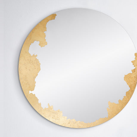 The gilded round mirror seen straight on, the hand applied gold leaf gathered down one side of the glass.