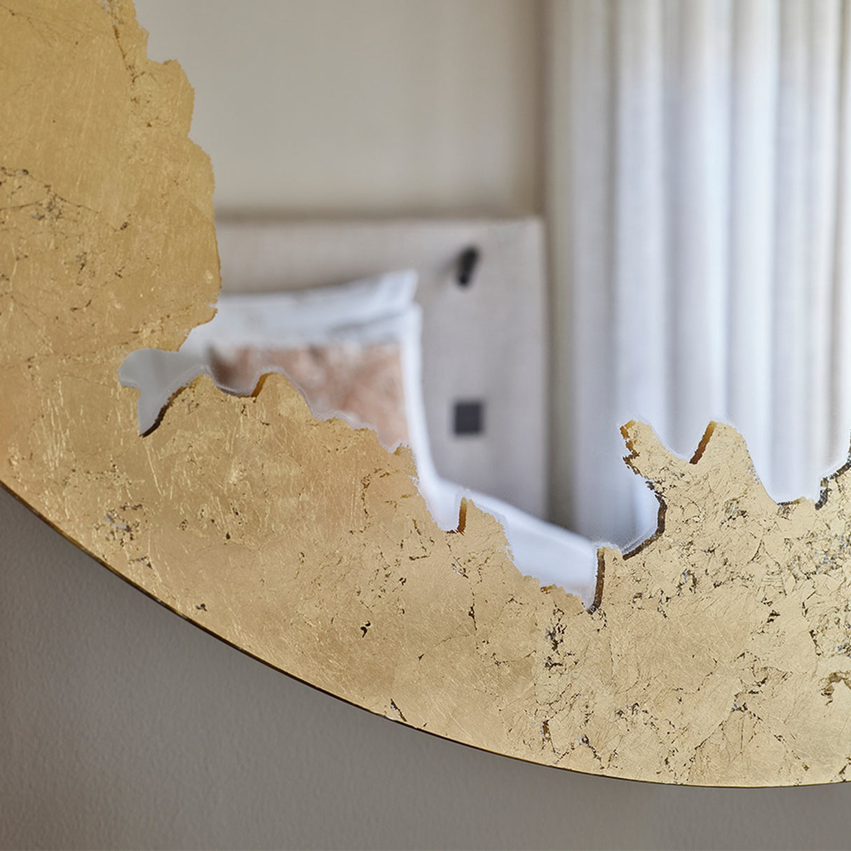 Close-up of the gold leaf edge in a bedroom, with the corner of a bed and its cushions carried in the reflection.