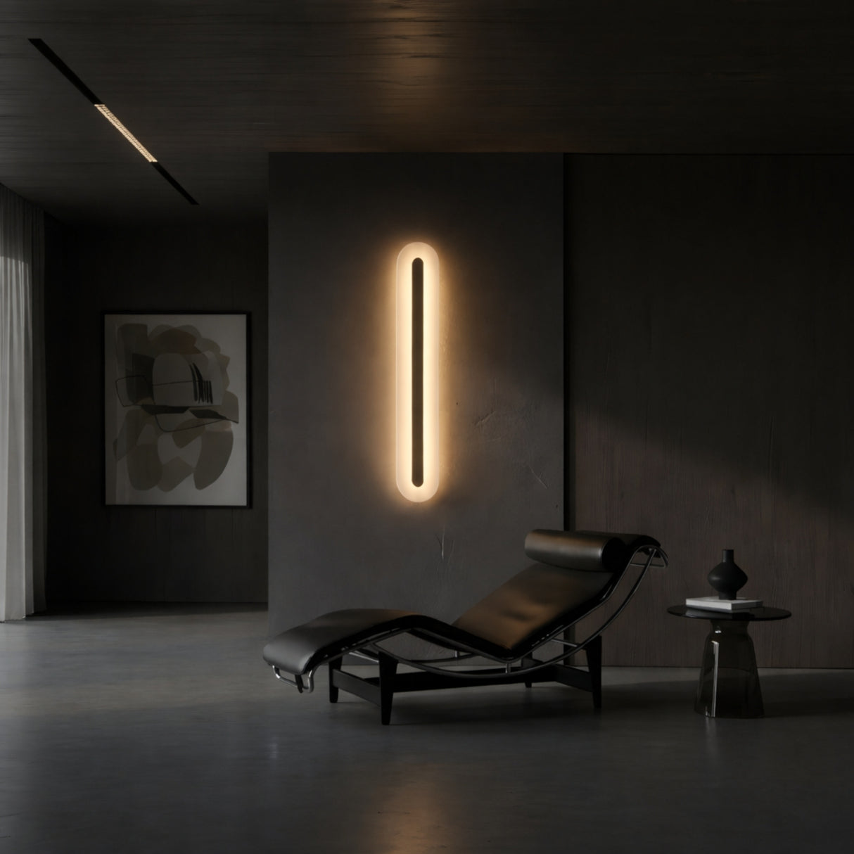A modern, minimalist room features a black leather chaise lounge, a small round side table with a vase, abstract wall art, and the Averra LED Extra Large Round Alabaster Wall Light in soft white & brass glowing on a dark gray wall.