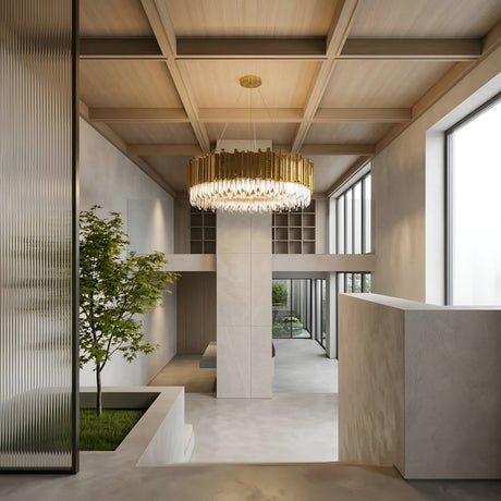 A modern interior with high ceilings, floor-to-ceiling windows, light wood paneling, a built-in planter featuring a small tree, minimalist white and grey walls, and the Royal 6-12 Crystal Light Chandelier - Gold as a striking centerpiece.
