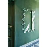 Wiggle Scalloped Edge Wall Mirror 133cm with wavy, frameless glass outline and engraved inner border, mounted on a green wall in a hallway beside a matching green door.
