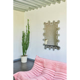 Wiggle Scalloped Edge Wall Mirror 133cm with a wavy, frameless glass outline and engraved inner border, mounted on a white wall above a pink sofa in a living room setting.