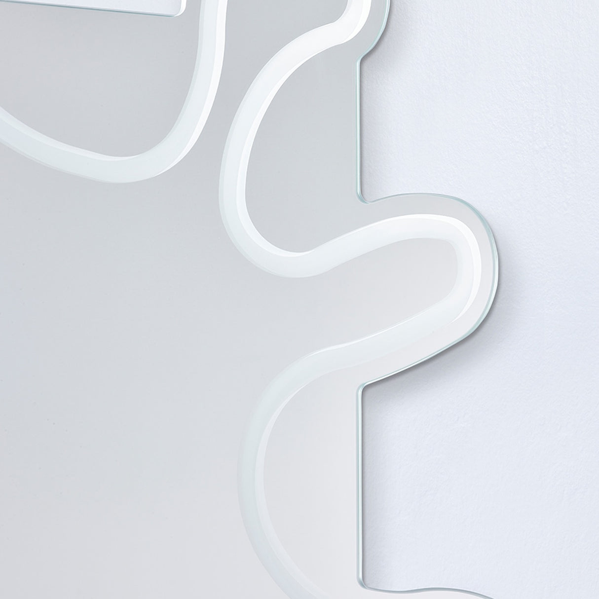 Close-up of the Wiggle Scalloped Edge Wall Mirror 133cm, showing the frameless glass edge with its wavy outline and engraved border line against a plain wall.