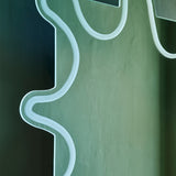 Close-up of the Wiggle Scalloped Edge Wall Mirror 133cm, frameless glass with a wavy irregular outline and an engraved border line just inside the edge, set against a green wall.