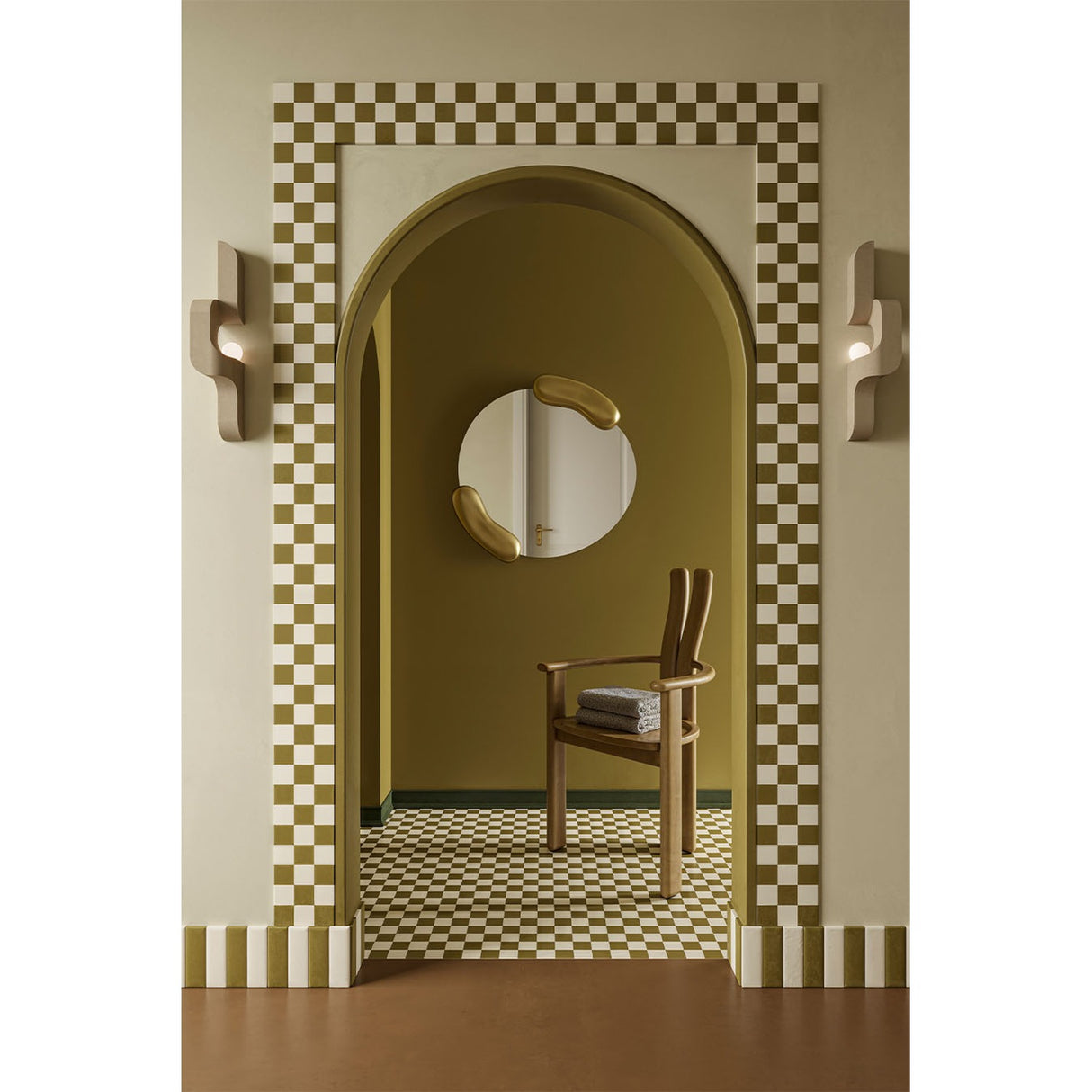 Calco Gold Leaf Sculpted Round Wall Mirror 73cm hung in a hallway, with organic gold-leaf forms at either side of the asymmetric glass, above a wooden armchair.
