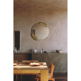 Calco Gold Leaf Sculpted Round Wall Mirror 73cm with organic asymmetric glass and two gold-leaf sculpted forms, shown above a marble console in a dining room setting.