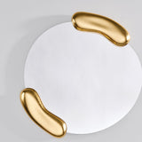 Calco Gold Round wall mirror, 73cm, with an asymmetric glass shape framed by two sculpted gold leaf forms holding it at opposite sides, shown against a plain light grey background.