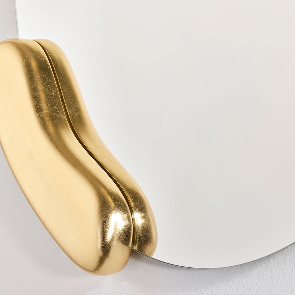 Calco Gold Round wall mirror, close-up of a sculpted gold leaf form appearing to hold the asymmetric mirror glass, set against a plain white background.