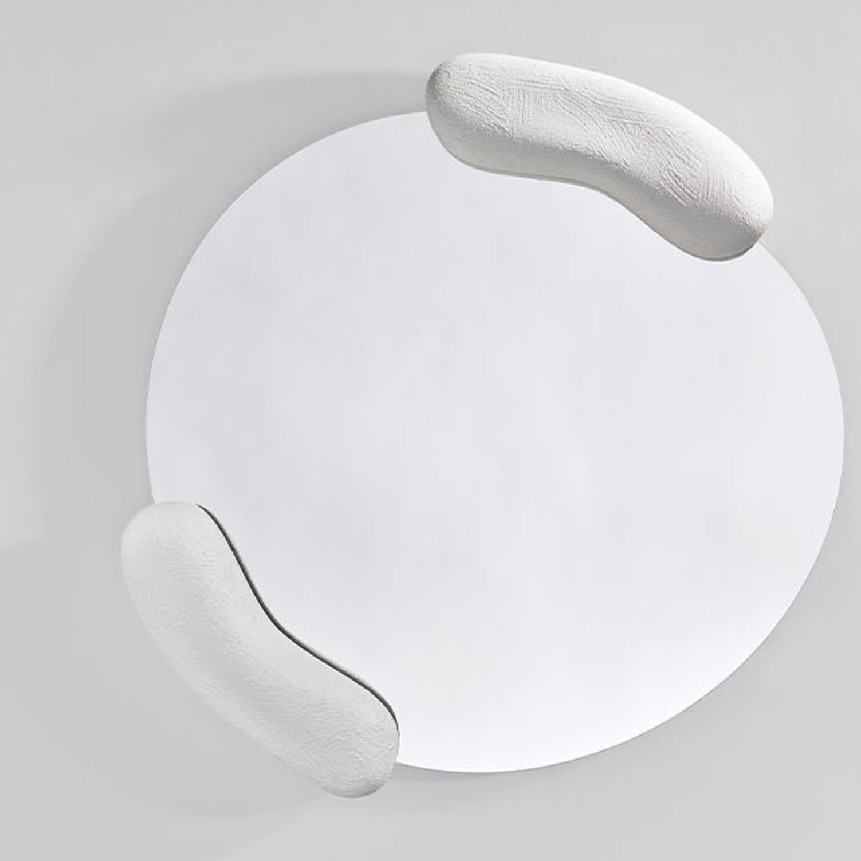 Calco White Sculpted Round Wall Mirror 73cm, with two textured white moulded forms holding opposite edges of an asymmetric glass, shown against a plain light grey background.
