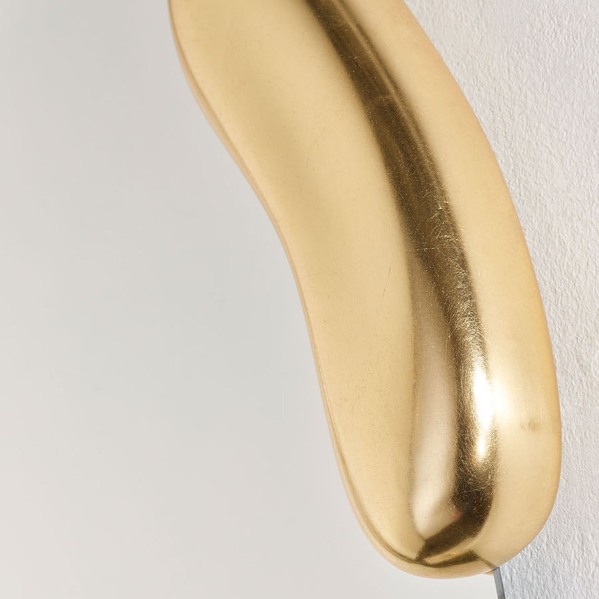 Close-up of the Calco Gold Leaf Sculpted Wall Mirror 116cm, showing the smooth, curved gold-leaf frame with an irregular organic shape against a plain light background.