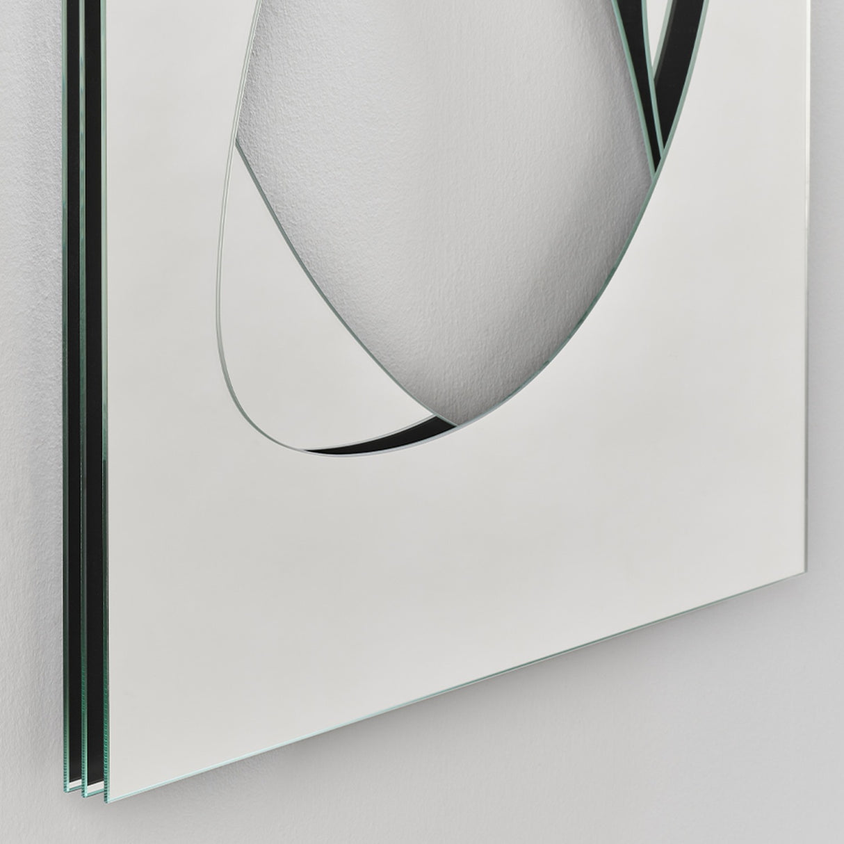 Angled close-up of the Infinito Precision Cut Void Wall Mirror 100cm, showing a white frameless panel with a layered glass edge and an organic cut void revealing mirrored depth beneath.