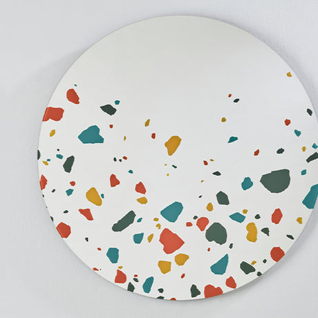 Terrazzo Round Printed Glass Wall Mirror 100cm, a frameless round mirror with red, teal, ochre and grey terrazzo chip print clustered at the lower edge, mounted on a light grey wall.