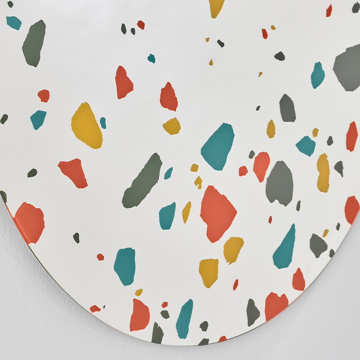 Terrazzo Round Printed Glass Wall Mirror 100cm, a frameless round mirror with red, teal, ochre and grey terrazzo chips printed on the silvered glass, denser near the lower edge.