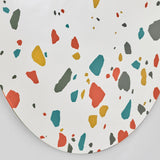 Terrazzo Round Printed Glass Wall Mirror 100cm, a frameless round mirror with red, teal, ochre and grey terrazzo chips printed on the silvered glass, denser near the lower edge.