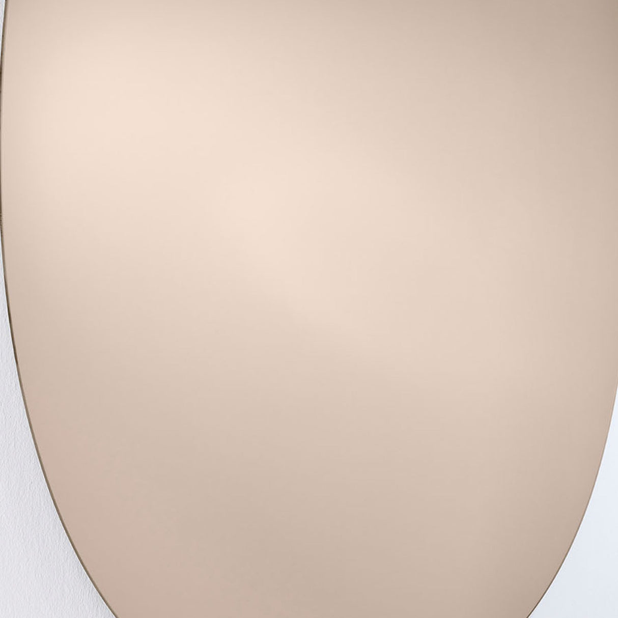 Close-up of the Oval Bronze Tinted Frameless Wall Mirror, 106cm, showing the bare polished glass edge and warm bronze-tinted surface against a plain wall.