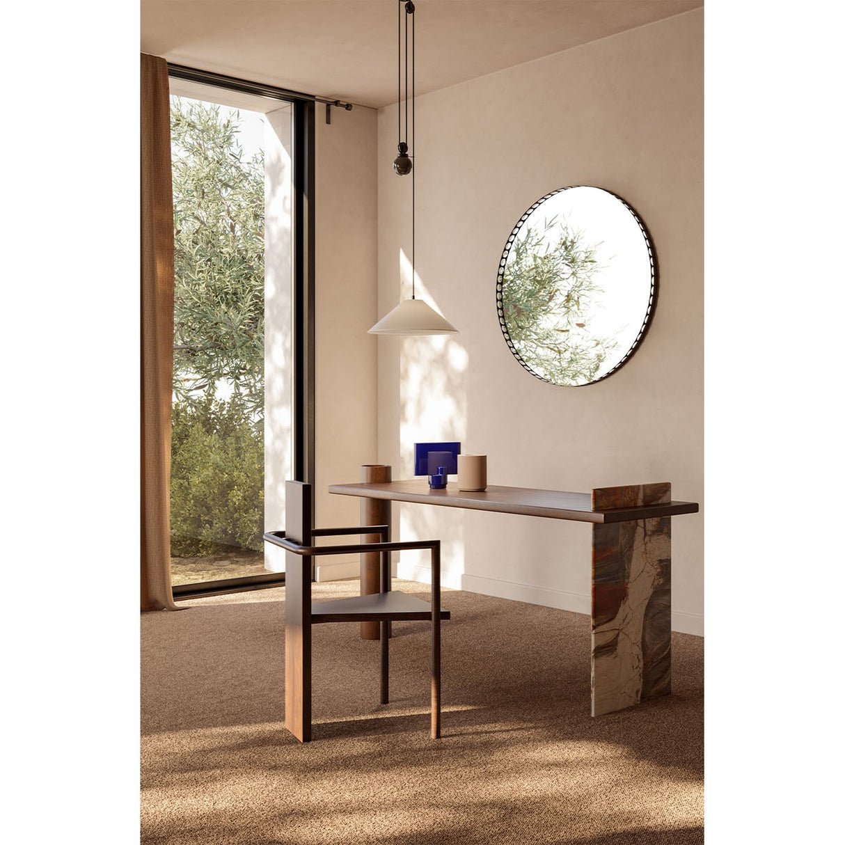 Reel Perforated Rim Round Wall Mirror 100cm in black, hung above a console table in a living space, reflecting greenery through a window.