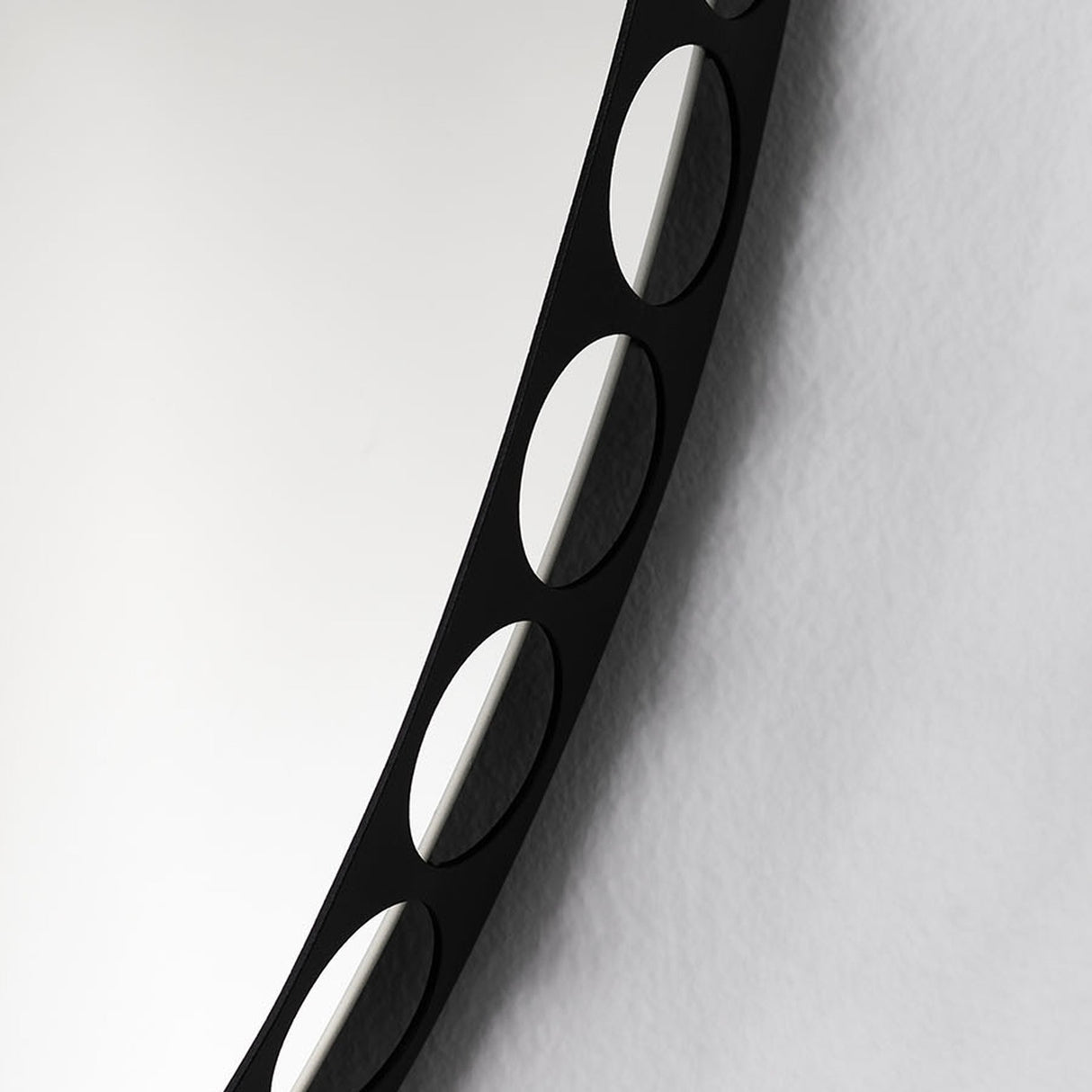 Close-up of the Reel round wall mirror's black metal rim, showing the row of perforated round cut-outs against a plain light background.