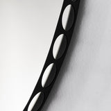Close-up of the Reel round wall mirror's black metal rim, showing the row of perforated round cut-outs against a plain light background.