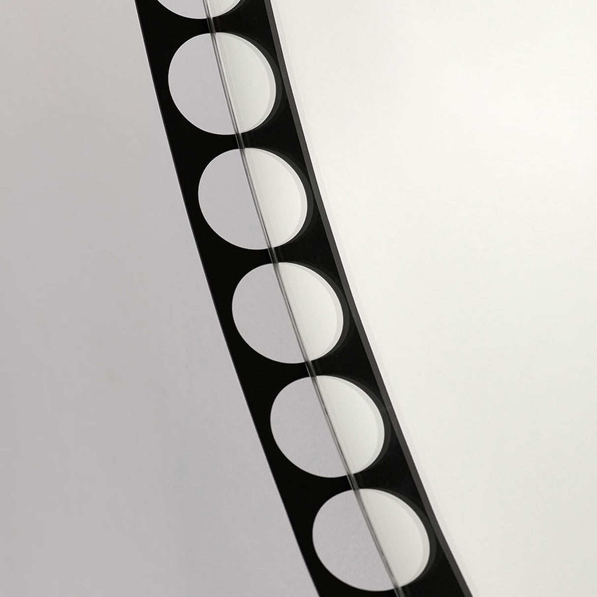 Close-up of the Reel Round Wall Mirror 100cm in black, showing the perforated metal rim with a row of round cut-out holes revealing the wall behind, set against a plain light background.