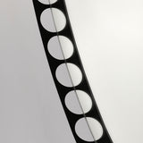 Close-up of the Reel Round Wall Mirror 100cm in black, showing the perforated metal rim with a row of round cut-out holes revealing the wall behind, set against a plain light background.