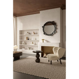 Round wall mirror with a black frameless border of overlapping printed glass bubbles, mounted above a fireplace in a living room with a shelving unit and cream armchair nearby.