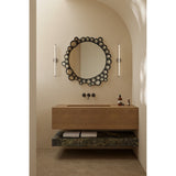 Round wall mirror with a black bubble-patterned glass frame of overlapping circles, hung above a wood vanity with wall-mounted taps in a bathroom setting.