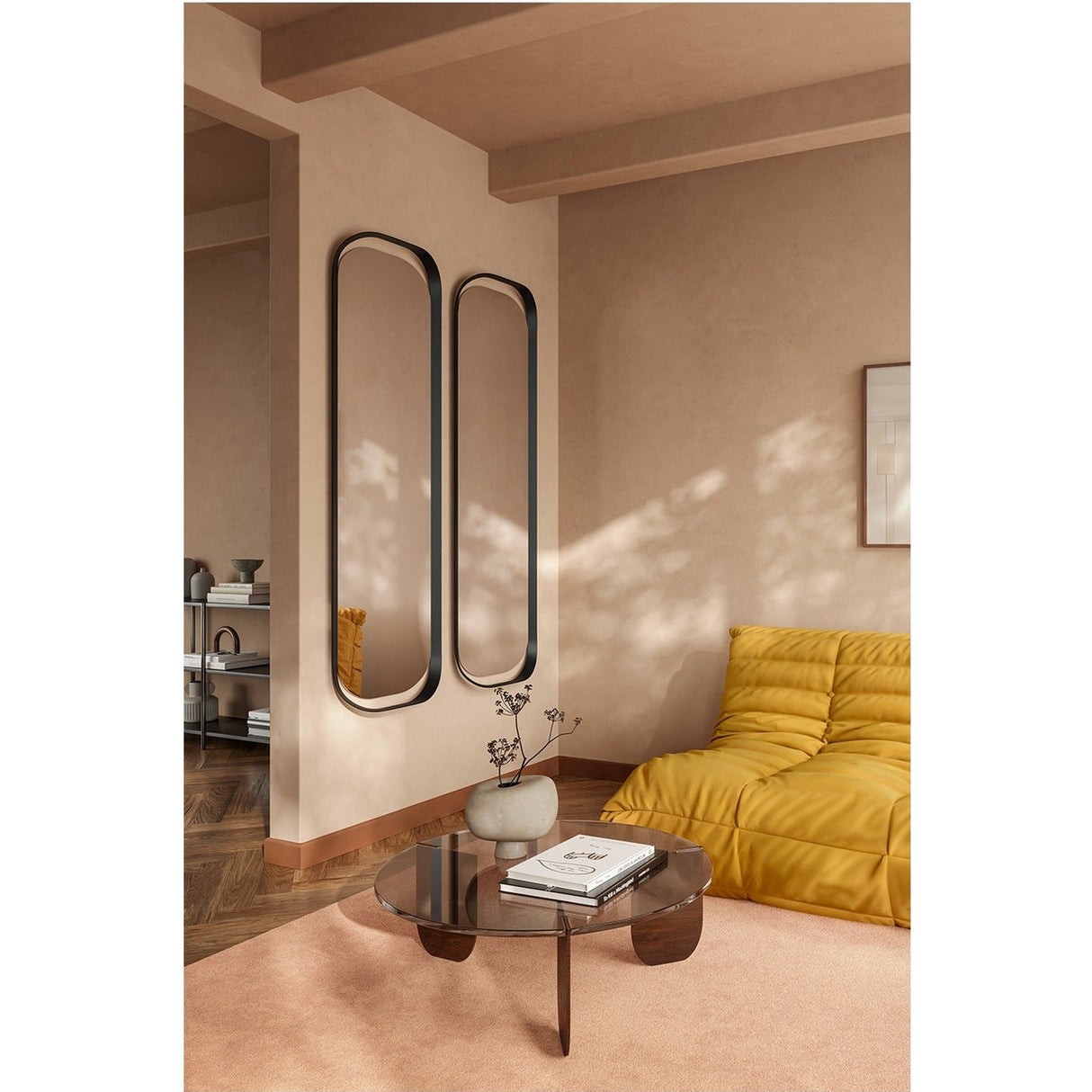Two Calligra curved black metal wall mirrors with elongated oval shapes hang side by side in a warm-toned living room beside a mustard sofa.