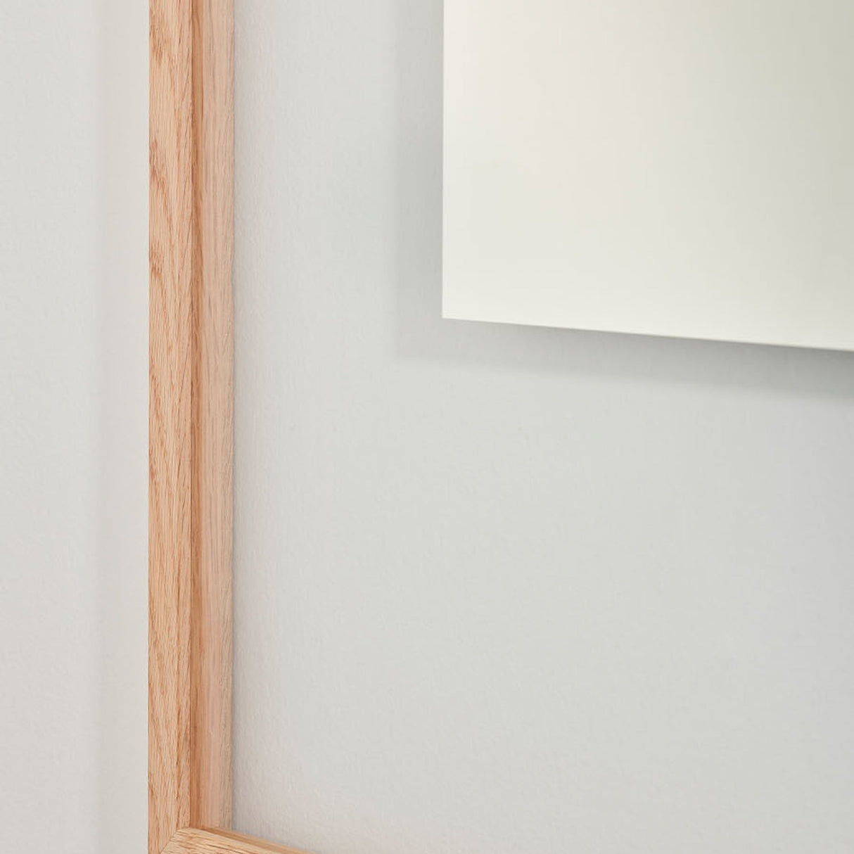 Close-up of the Passepartout Square Wall Mirror's solid oak frame corner, showing the natural wood grain against a plain light grey wall.