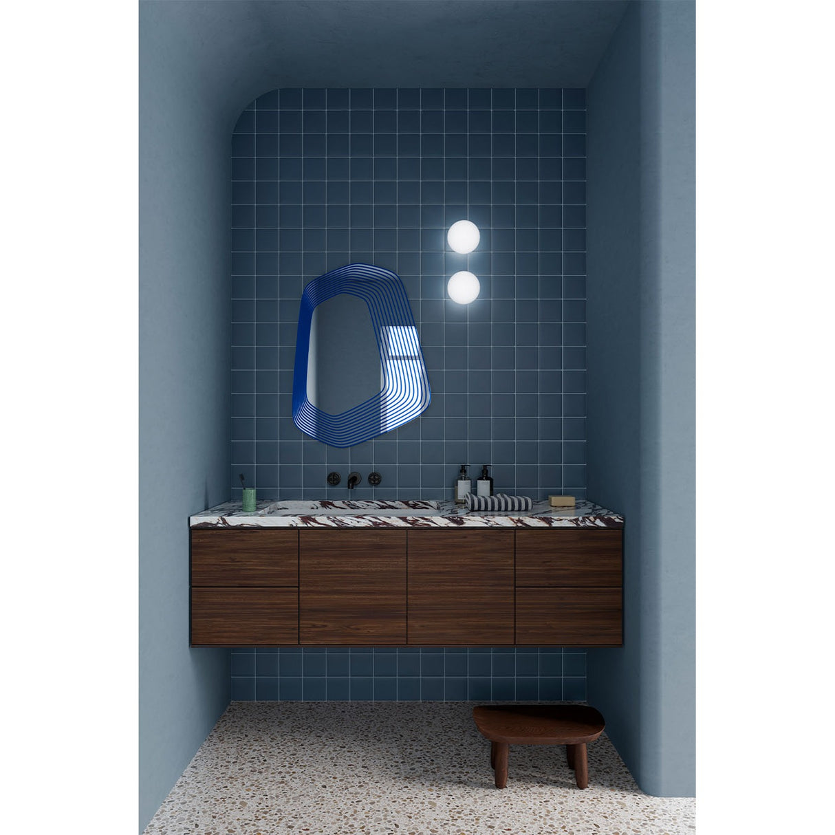 Vibe Blue Line Print Irregular Wall Mirror 80cm with a five-sided frameless outline, shown above a dark wood vanity in a blue-tiled bathroom.