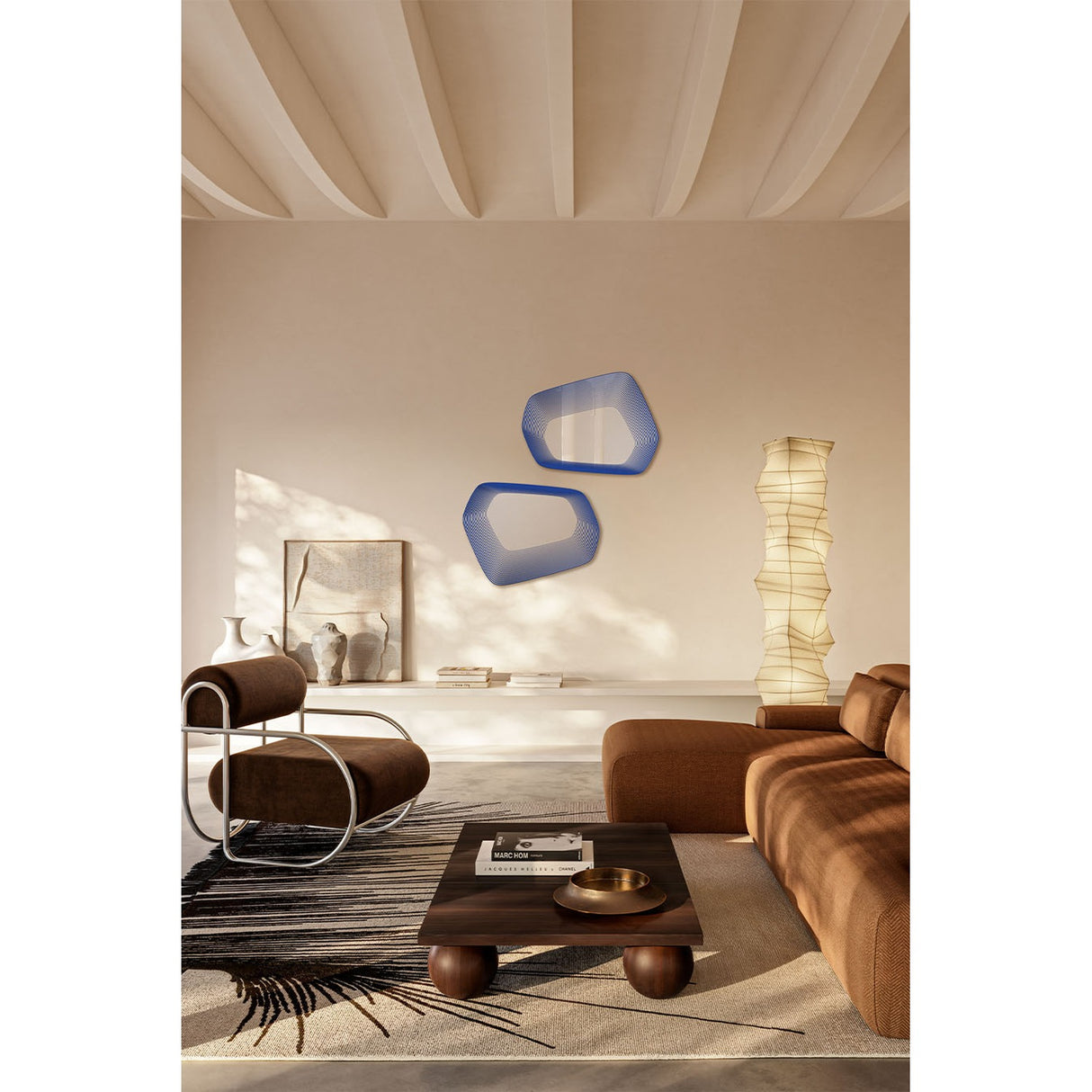 Two Vibe Blue irregular wall mirrors with concentric blue line prints and soft five-sided outlines, shown above a sideboard in a living room with a floor lamp and brown sofa.