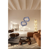 Two Vibe Blue irregular wall mirrors with concentric blue line prints and soft five-sided outlines, shown above a sideboard in a living room with a floor lamp and brown sofa.