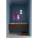 Vibe Pink Line Print Irregular Wall Mirror 80cm, an irregular frameless mirror with concentric magenta line detailing, shown above a dark wood vanity in a bathroom setting.