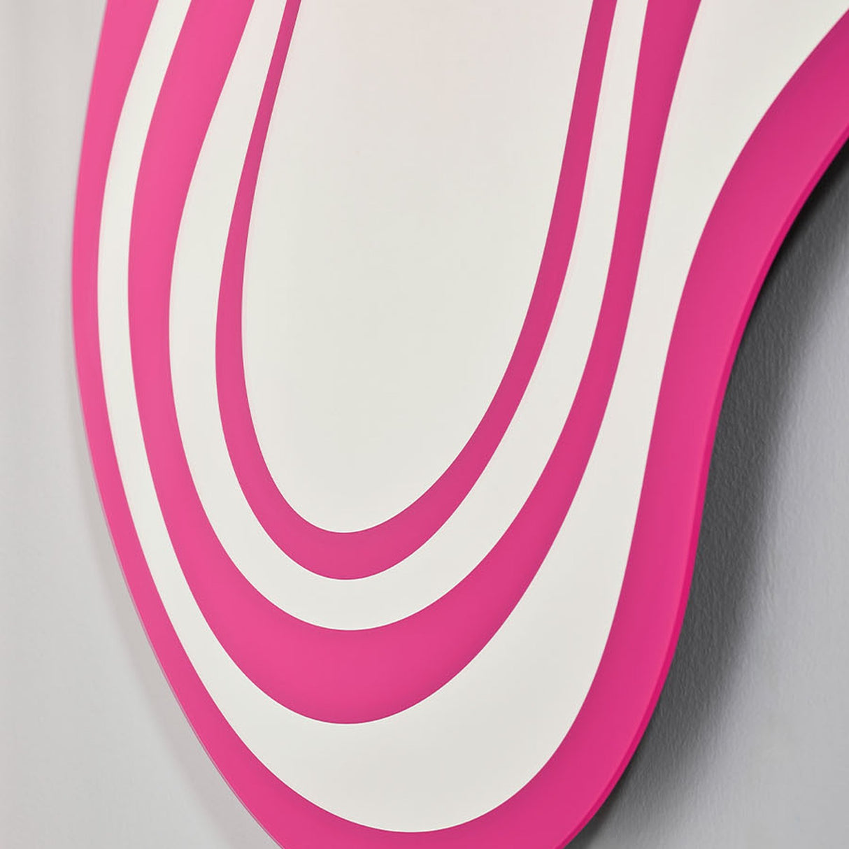 Close-up of Nimbus Pink Banded Glass Wall Mirror, irregular cloud-like outline with concentric pink and mirrored glass bands, frameless, against a plain grey wall.